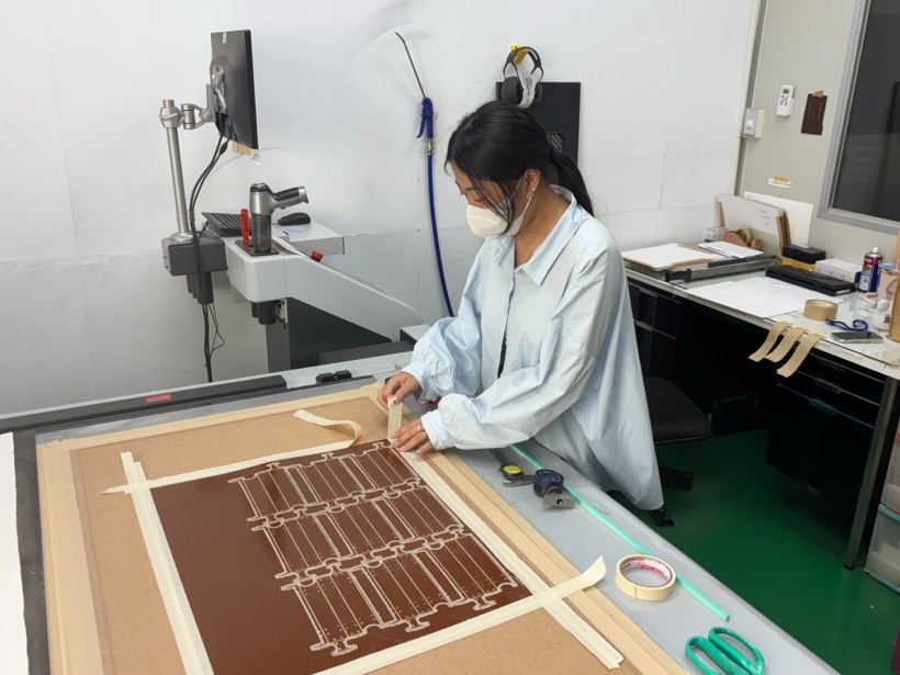 實習生在割樣機台上固定材料，準備割樣